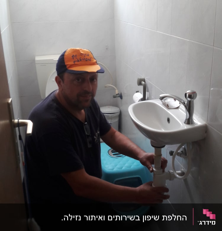 אדם מתקן צנרת מתחת לכיור בחדר אמבטיה